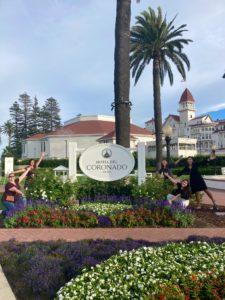 Hunt staff gather around the Hotel Del Coronado sign, waving their arms and smiling at the camera.